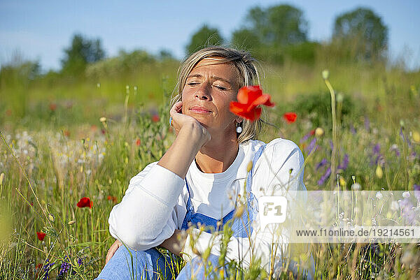 Woman with hand on chin sitting amidst flowers in meadow