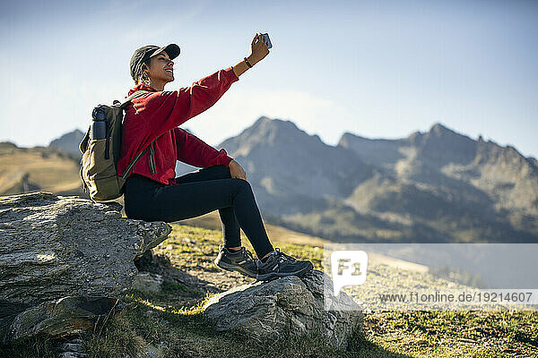 Young woman sitting on rock taking selfie through smart phone