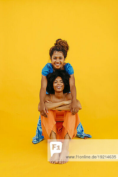 Happy multiracial friends sitting against yellow background