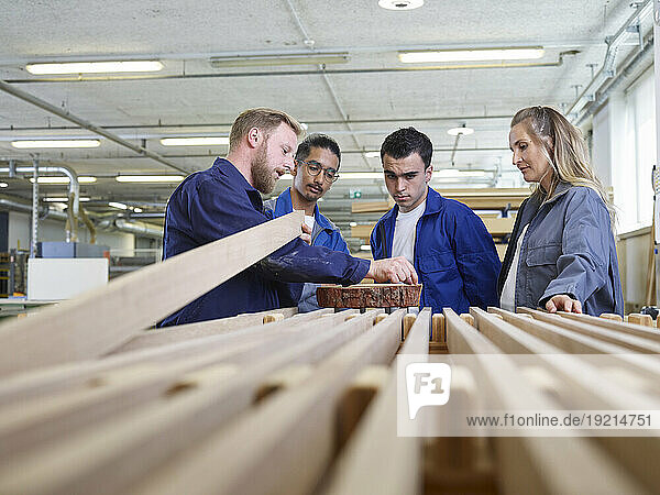 Carpenter teaching trainees about wood quality in factory