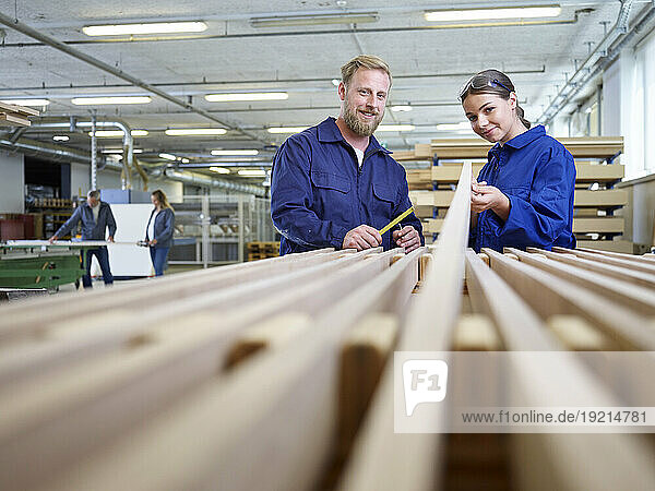 Smiling carpenter and trainee at factory