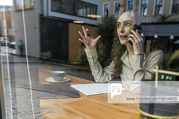 Businesswoman talking on smart phone at cafe seen through cafe