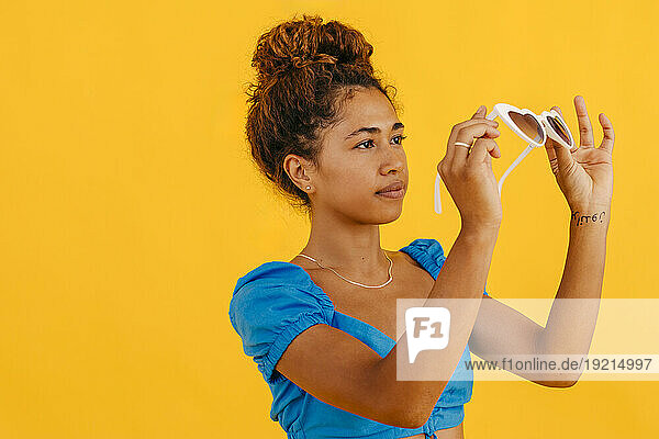 Woman holding sunglasses against yellow background