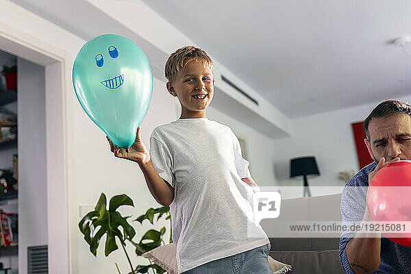 Smiling boy with balloon standing by father at home