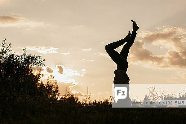 Silhouette of woman practicing headstand yoga at sunset