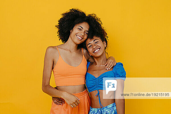 Happy young multiracial friends standing against yellow background
