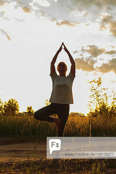 Mature woman practicing tree pose yoga at sunset