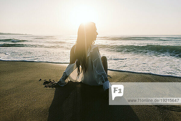 Woman sitting on sand near sea at dawn