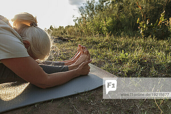 Mature woman practicing yoga on mat at sunset