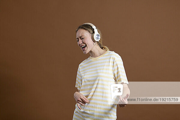 Woman imitating guitar and enjoying music on headphones against brown background