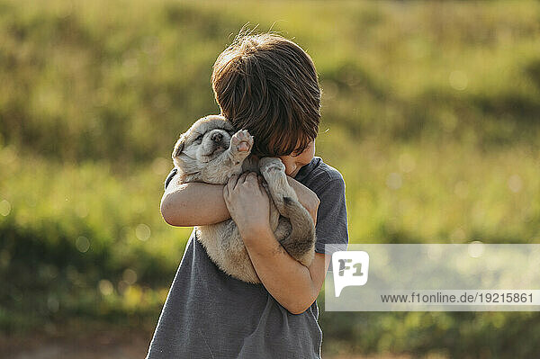 Boy embracing cute mixed breed puppy at meadow