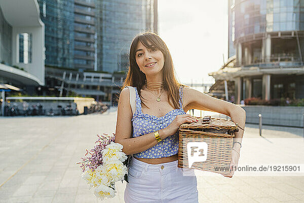 Smiling woman with bouquet of flowers and basket on sunny day