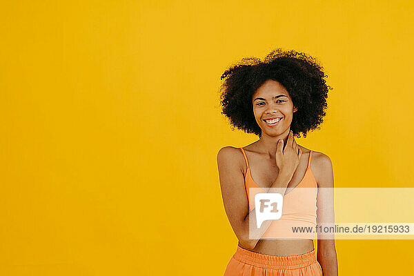 Smiling woman touching neck standing against yellow background