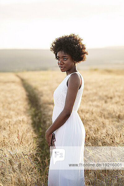 Thoughtful young woman standing in wheat field at sunset