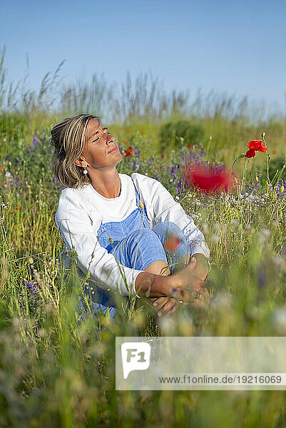 Woman with eyes closed sitting in meadow