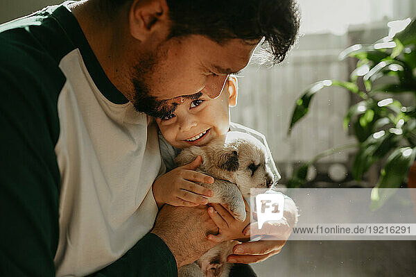 Smiling man holding son and cute puppy at home