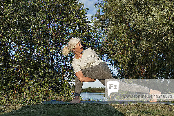 Flexible woman practicing yoga on mat at lakeshore