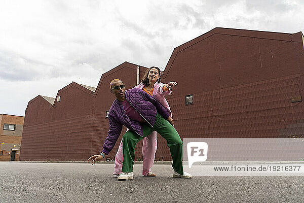 Happy woman dancing with friend in front of building