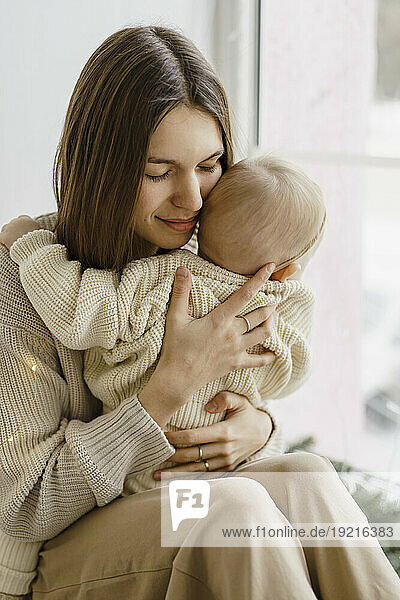 Happy mother carrying baby daughter near window at home