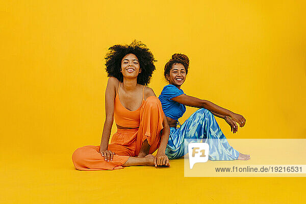 Smiling young friends sitting against yellow background