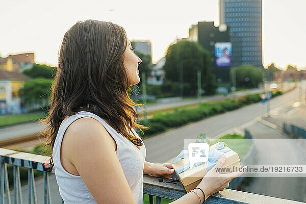 Thoughtful woman standing with gift box by railing