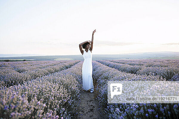 Happy woman with arms raised standing amidst lavender field