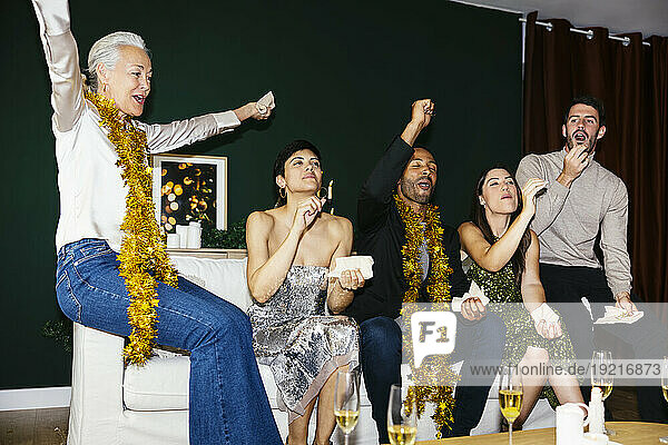 Happy multi-generation family cheering on sofa while celebrating new year at home