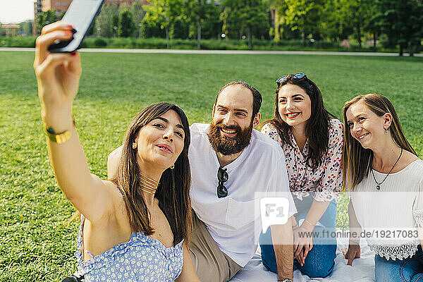 Happy woman taking selfie through smart phone with friends