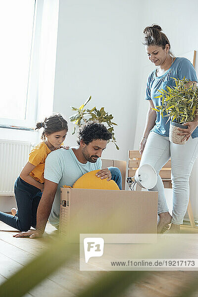 Woman holding plant with man and daughter packing cushion in box
