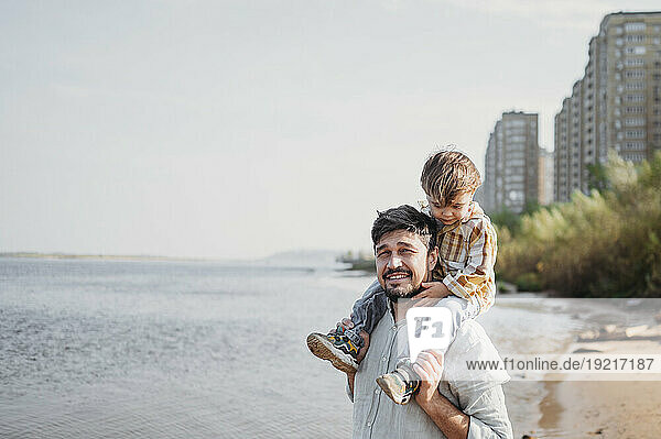 Smiling father carrying son on shoulders at beach
