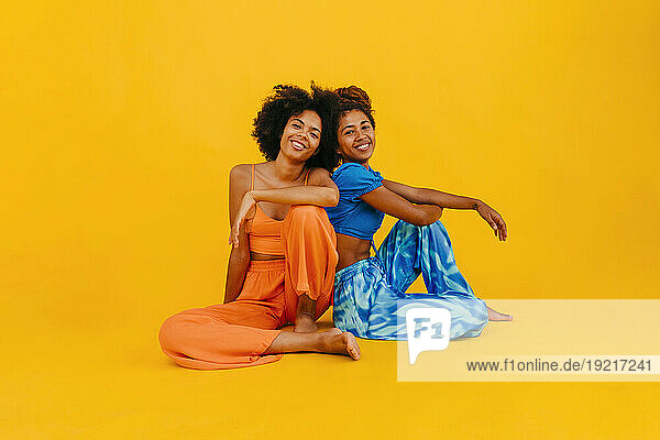 Young friends sitting against yellow background