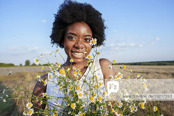 Smiling woman holding bunch of daises in field on sunny day
