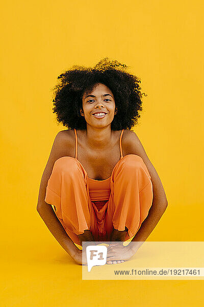 Smiling young woman with curly hair crouching against yellow background