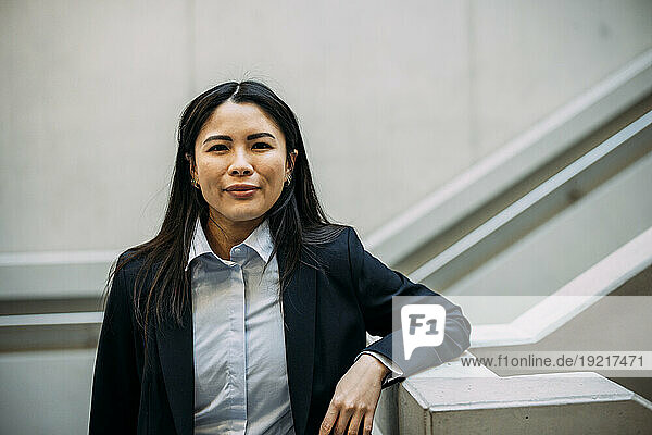 Smiling businesswoman leaning on staircase railing at workplace