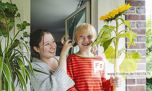 Happy girl with big sunflower standing by sister on balcony