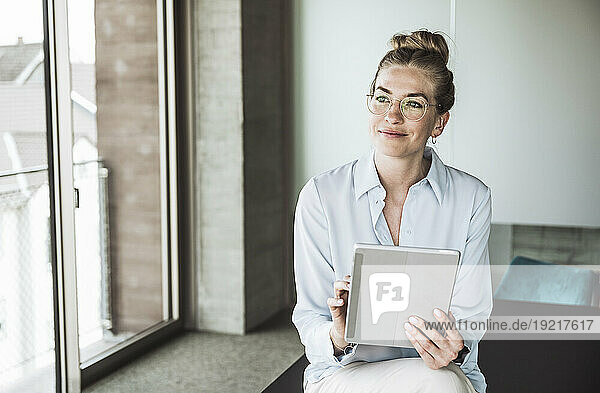 Thoughtful businesswoman wearing eyeglasses and sitting with tablet PC on desk