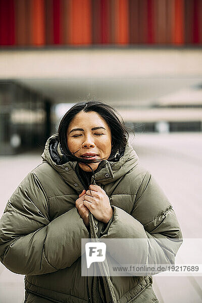 Businesswoman with eyes closed wearing padded jacket outside office building
