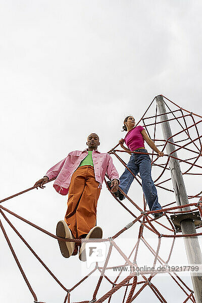 Couple spending leisure time on jungle gym under sky