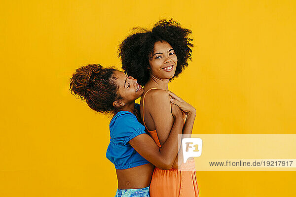 Smiling woman embracing young friend against yellow background