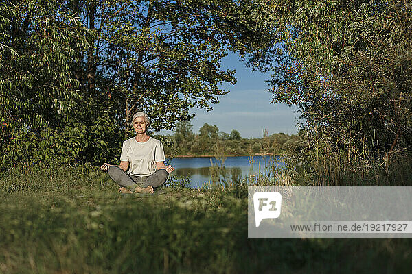 Mature woman practicing lotus position and meditating at lakeshore