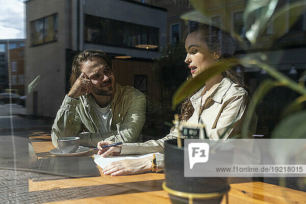 Businesswoman discussing with colleague at table in cafe seen through glass