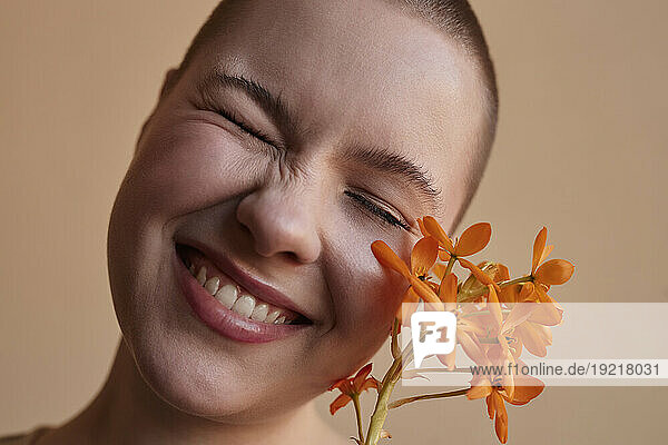 Happy woman with eyes closed by flower against beige background