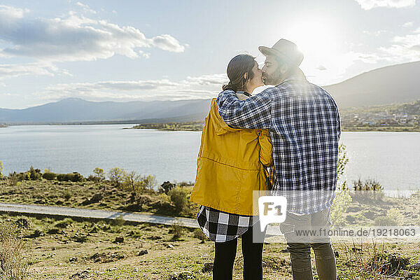 Affectionate couple kissing near lake on sunny day