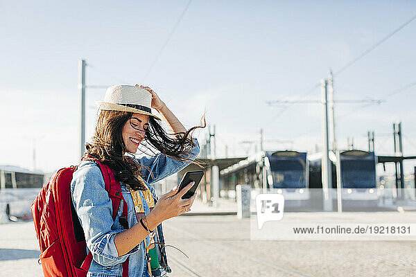 Happy woman wearing hat using smart phone on sunny day