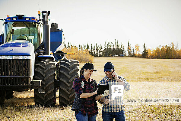 Husband and wife using portable wireless devices to manage and monitor their canola harvest and making a call while standing in front of a big tractor; Alcomdale  Alberta  Canada