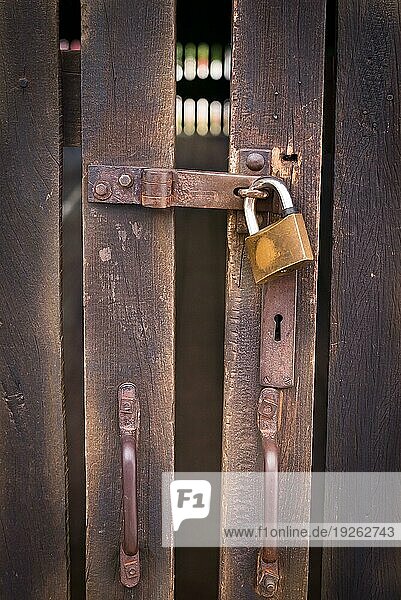 Nahaufnahme eines Vorhängeschlosses mit einer alten Metallfalle und einer Heftklammer an einer alten Holztür