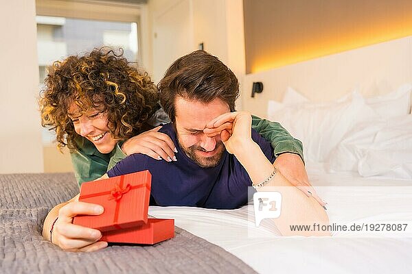 Valentinstag  ein junges kaukasisches Paar im Schlafanzug auf dem Bett  die Braut überrascht ihren Freund mit einem netten Geschenk