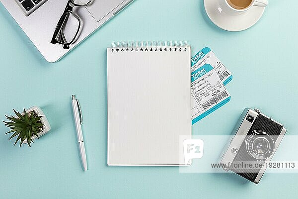 Blanko Spirale Notizblock mit Flugtickets mit Laptop Brille Stift Kamera Kaffeetasse blau Schreibtisch umgeben