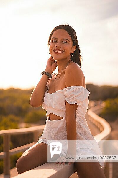 Eine junge brünette Kaukasierin im Urlaub am Strand in einem weißen Sommerkleid  die sich auf dem Holzsteg amüsiert