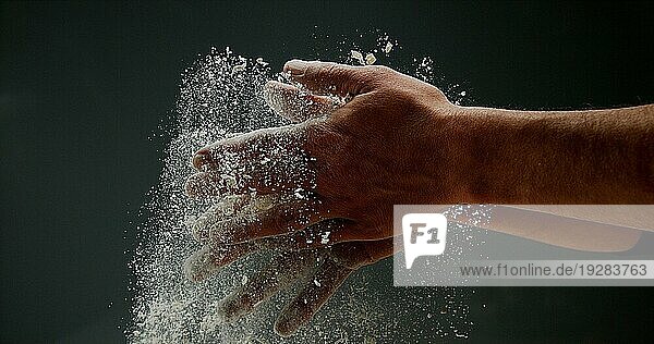 Hände eines Mannes mit Mehl vor schwarzem Hintergrund